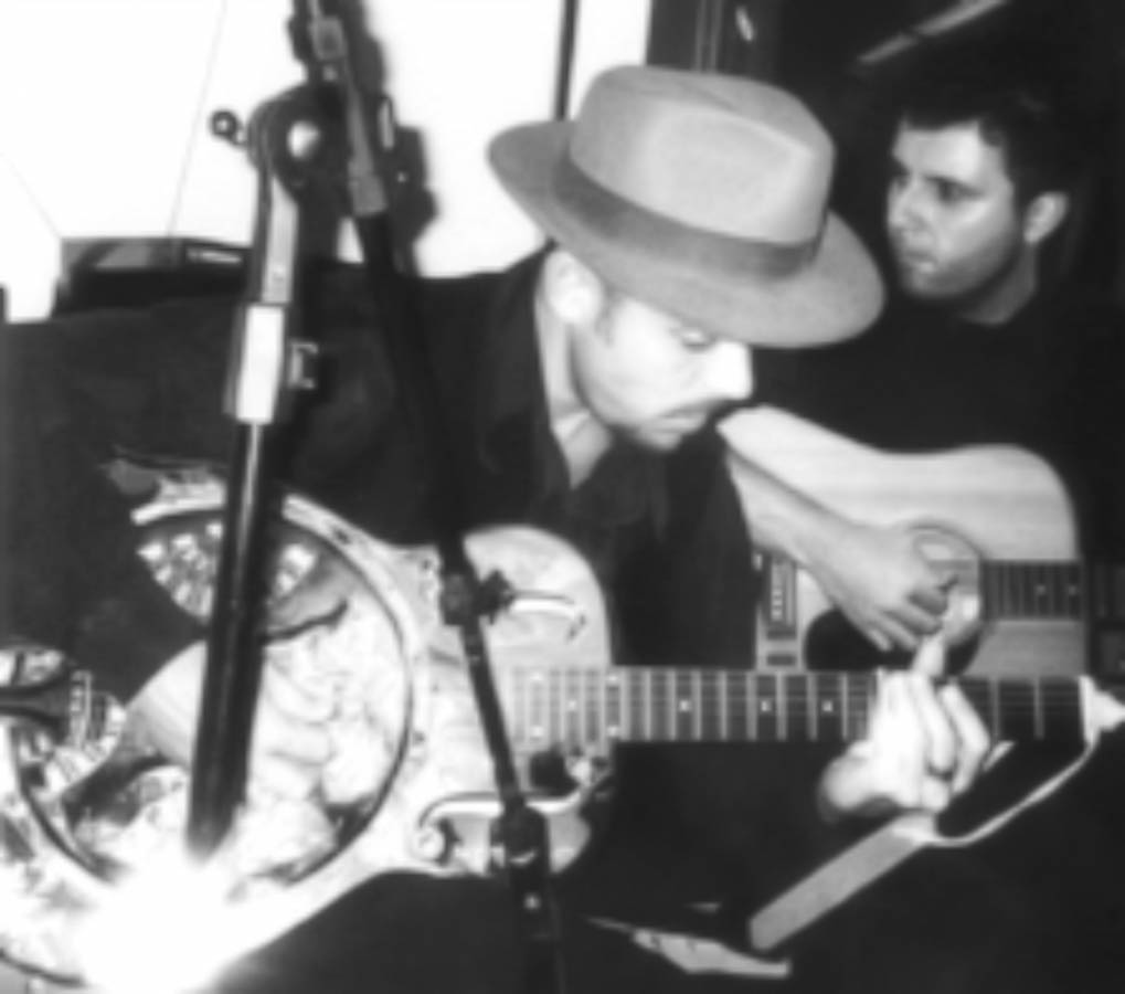 Eduardo Sardinha e Luiz Carlos Big em fotografia preto e branco do Bluescake, com guitarra de corpo metálico ou ressonador em primeiro plano e violão ao fundo. Elementos visíveis: duo, guitarristas, chapéu, instrumentos de cordas, amplificador, microfone, contraste e atmosfera de blues. Arquivo: Eduardo Sardinha / Sardinha17.