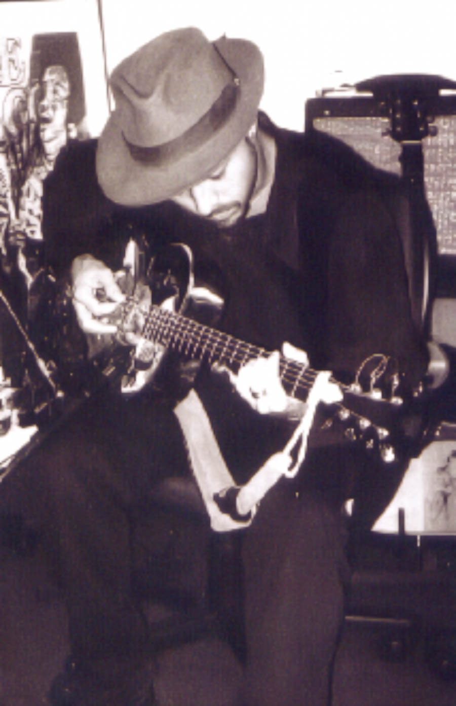 Retrato vertical preto e branco de músico do Bluescake tocando guitarra diante de amplificador. Elementos visíveis: guitarrista, chapéu, guitarra elétrica, amplificador, instrumento de cordas, luz e sombra, contraste e atmosfera de blues. Bluescake: Eduardo Sardinha e Luiz Carlos Big. Arquivo: Eduardo Sardinha / Sardinha17.