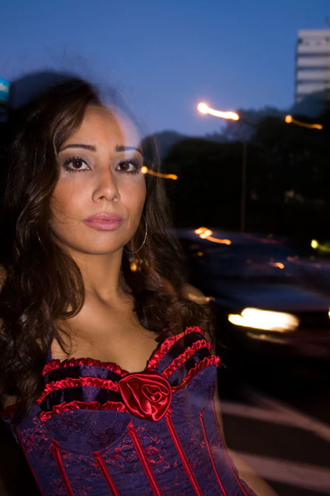 Retrato feminino urbano e noturno de Karla Jacobina, com corset azul e vermelho, automóvel, iluminação de rua e rastros de luz. Fotografia autoral de Eduardo Sardinha — Sardinha17. Palavras-chave: Karla Jacobina, retrato, fotografia noturna, cidade, trânsito, corset, azul, vermelho, luzes urbanas.