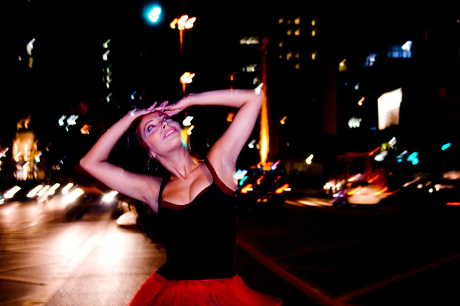 Fotografia noturna de Karla Jacobina em pose de dança, usando saia vermelha diante de trânsito e iluminação urbana. Fotografia autoral de Eduardo Sardinha — Sardinha17. Palavras-chave: dança, movimento, saia vermelha, longa exposição, cidade, retrato feminino.