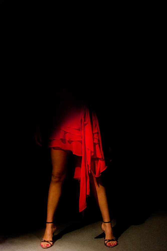 Composição vertical de figurino com saia vermelha assimétrica, pernas e sapatos pretos de dança contra fundo escuro, com iluminação dramática. Fotografia autoral de Eduardo Sardinha — Sardinha17. Palavras-chave: dança, figurino, saia vermelha, sapatos, moda, contraste, movimento.