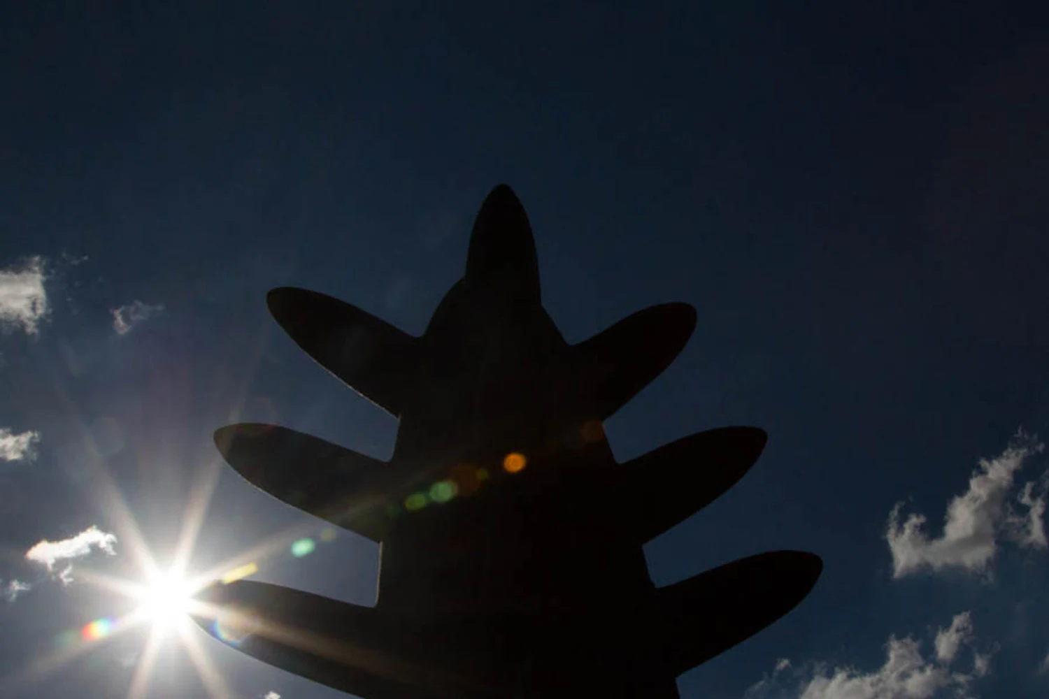 Escultura de Kimi Nii fotografada em contraluz, formando silhueta de volumes pontiagudos contra o céu. Elementos visíveis: cerâmica, escultura, espinhos, silhueta, sol, flare, céu azul, nuvens, alto contraste e perspectiva baixa. Fotografia autoral de Eduardo Sardinha / Sardinha17 para a Eurobike. Contexto: São Paulo, SP, Brasil.