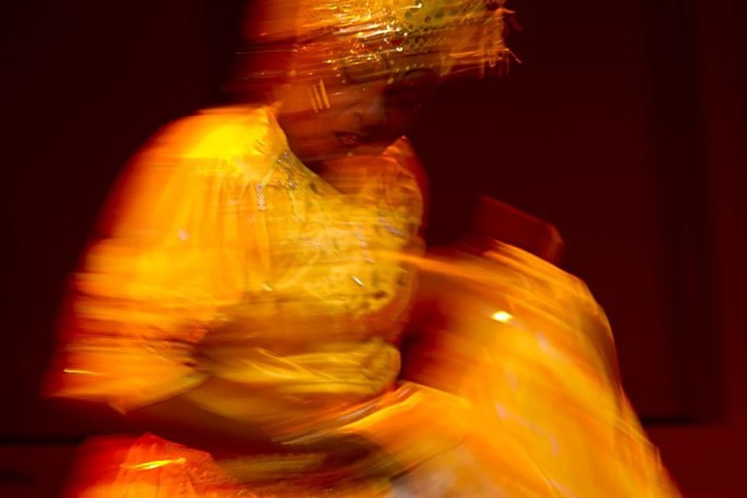 Dançarina do Yoruba Andabo gira em figurino amarelo, com desfoque de movimento e iluminação quente.
