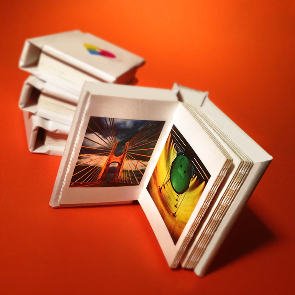 Pilha de minibooks com fotografias coloridas sobre fundo laranja intenso, em composição de produto.