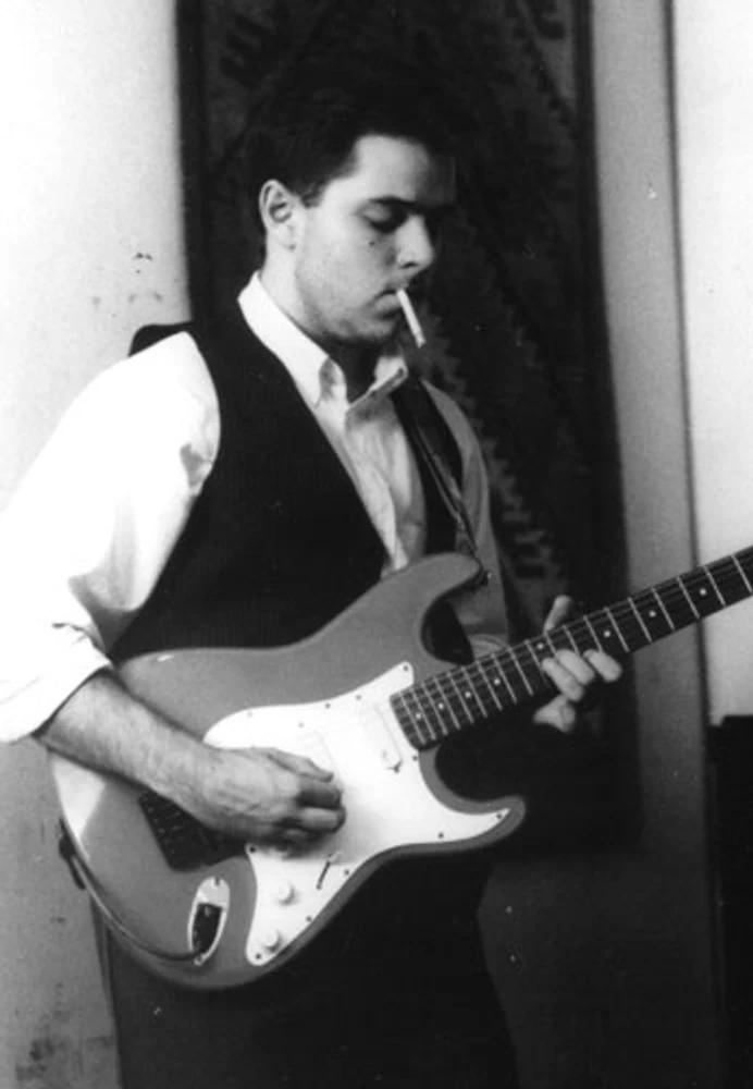 Eduardo Sardinha toca guitarra elétrica em fotografia vertical preto e branco da Mississampa Blues Band. Elementos visíveis: guitarrista, guitarra elétrica, cigarro, camisa branca, colete escuro, instrumento de cordas, retrato musical e textura analógica. Fotografia e arquivo autoral de Eduardo Sardinha / Sardinha17.
